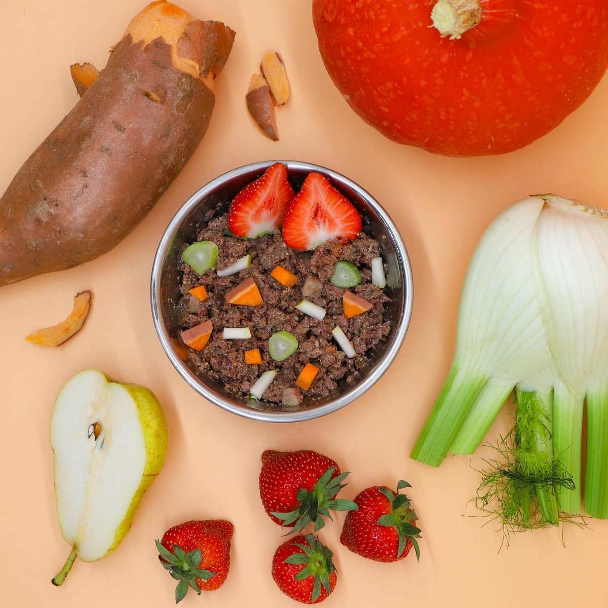 Nassfutter für Welpen mit Rind, Süßkartoffeln, Gemüse und Früchten, dekorativ arrangiert mit frischen Zutaten wie Kürbis, Fenchel und Erdbeeren.